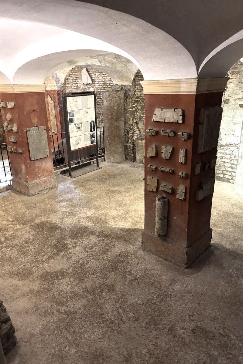 Crypte voûtée avec pilier en brique rouge et fragments lapidaires exposés