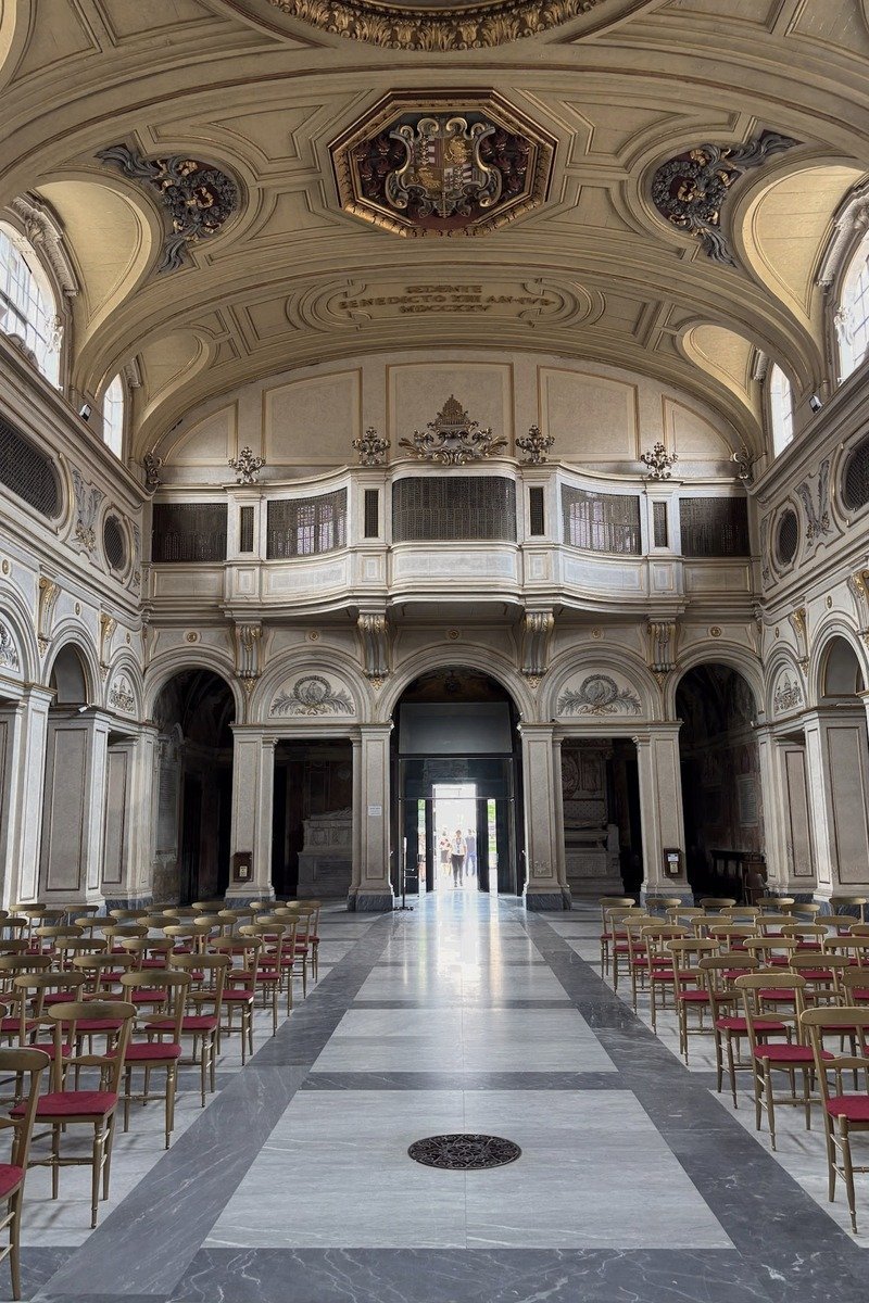 Nef baroque avec rangées de chaises dorées aux coussins rouges et plafond ornemental