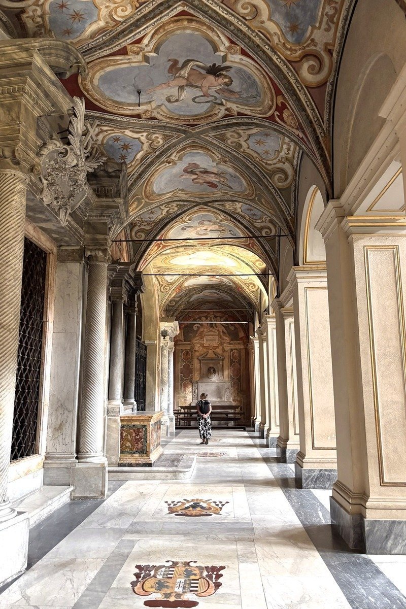 Porche voûté orné de fresques avec colonnes de marbre et visiteur solitaire