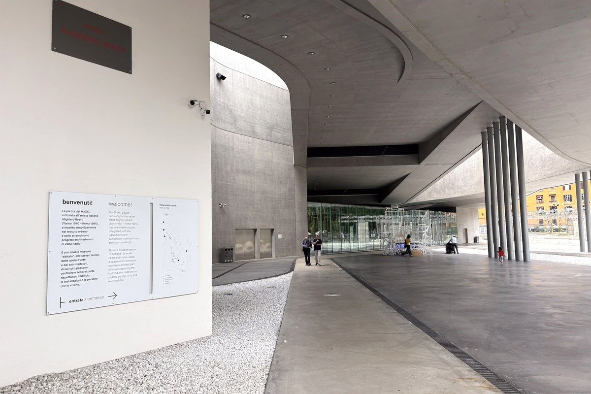 Parvis couvert d'un musée contemporain avec panneau d'accueil bilingue