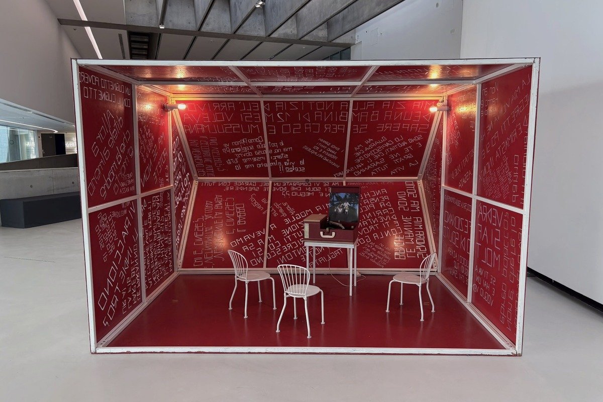 Installation artistique en forme de cabine rouge couverte de textes blancs