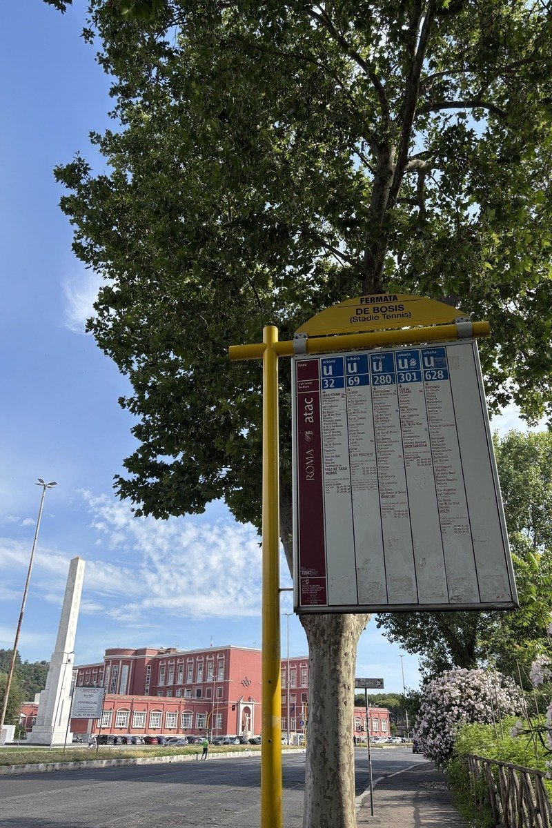 Panneau d'arrêt de bus jaune avec horaires ATAC sous un grand arbre