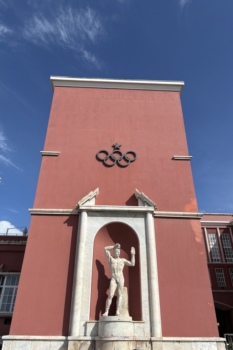 Façade rouge avec anneaux olympiques et statue de marbre en niche
