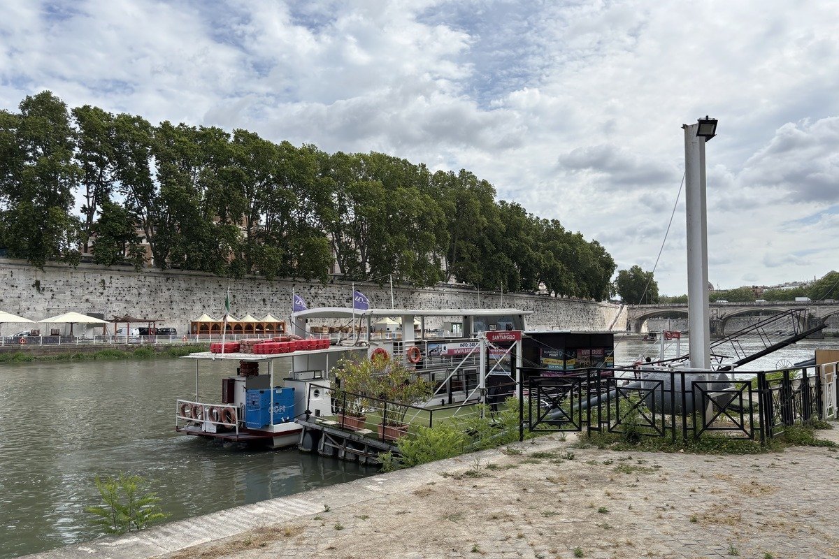 Péniche amarrée sur un fleuve, quai en pierre et arbres en fond