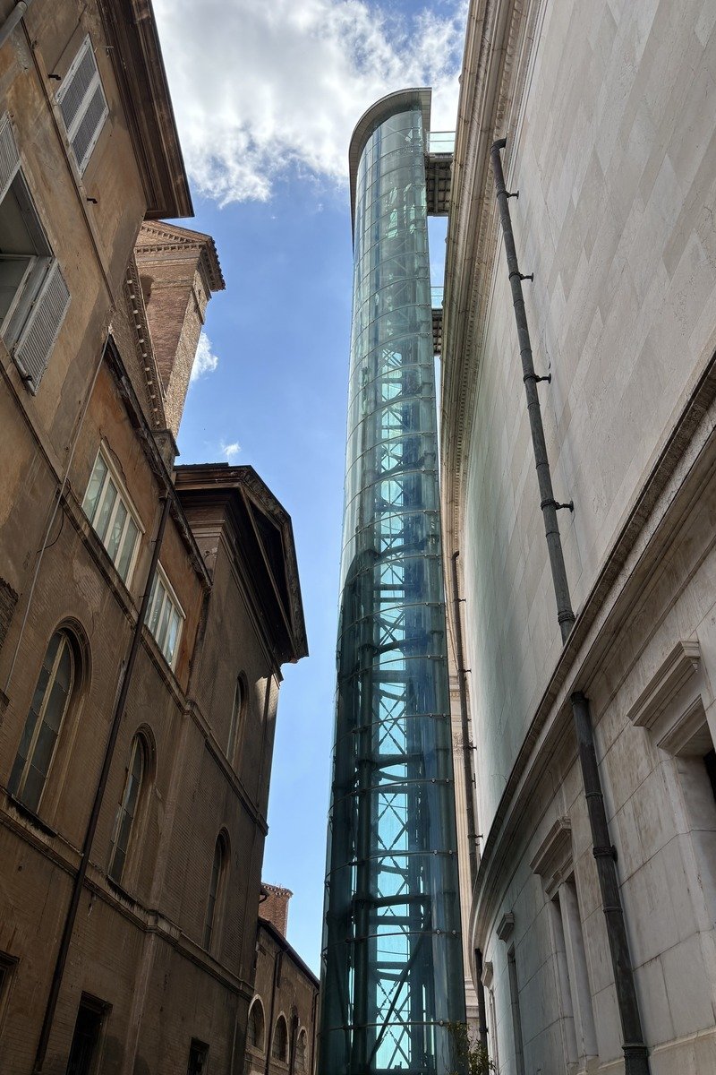Tour ascenseur cylindrique en verre entre deux bâtiments anciens