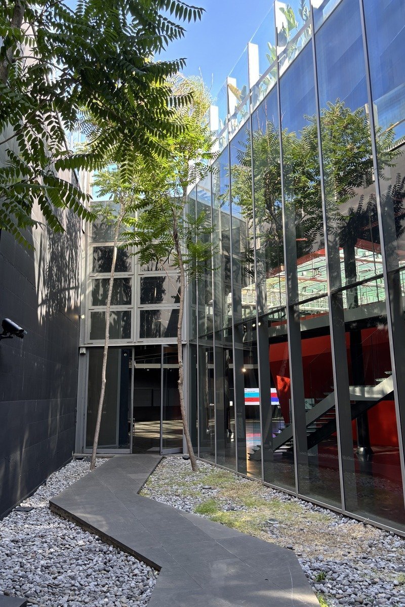 Cour intérieure avec façade vitrée reflétant des arbres et ciel bleu