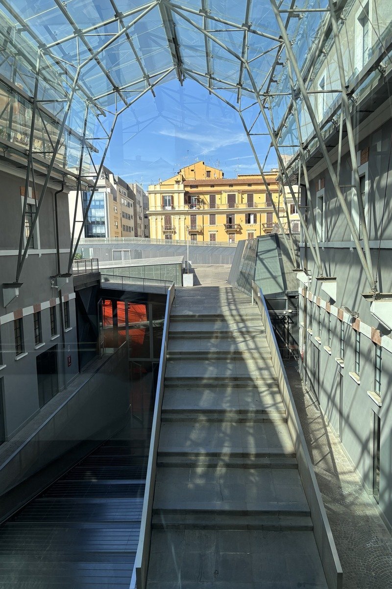 Escalier moderne sous verrière métallique avec immeuble ocre en arrière-plan