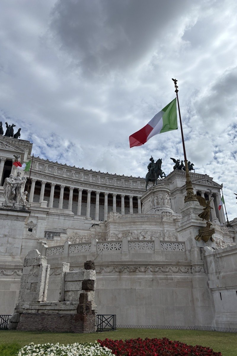 Monument en marbre blanc avec drapeau italien flottant sous ciel nuageux