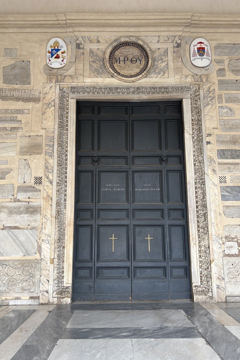 Grande porte sombre à panneaux avec deux croix dorées et encadrement en marbre