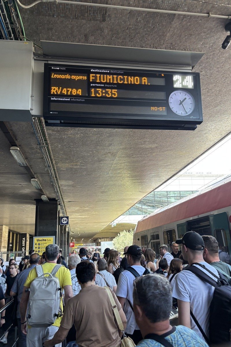 Foule de voyageurs sur un quai sous un panneau d'affichage de départ