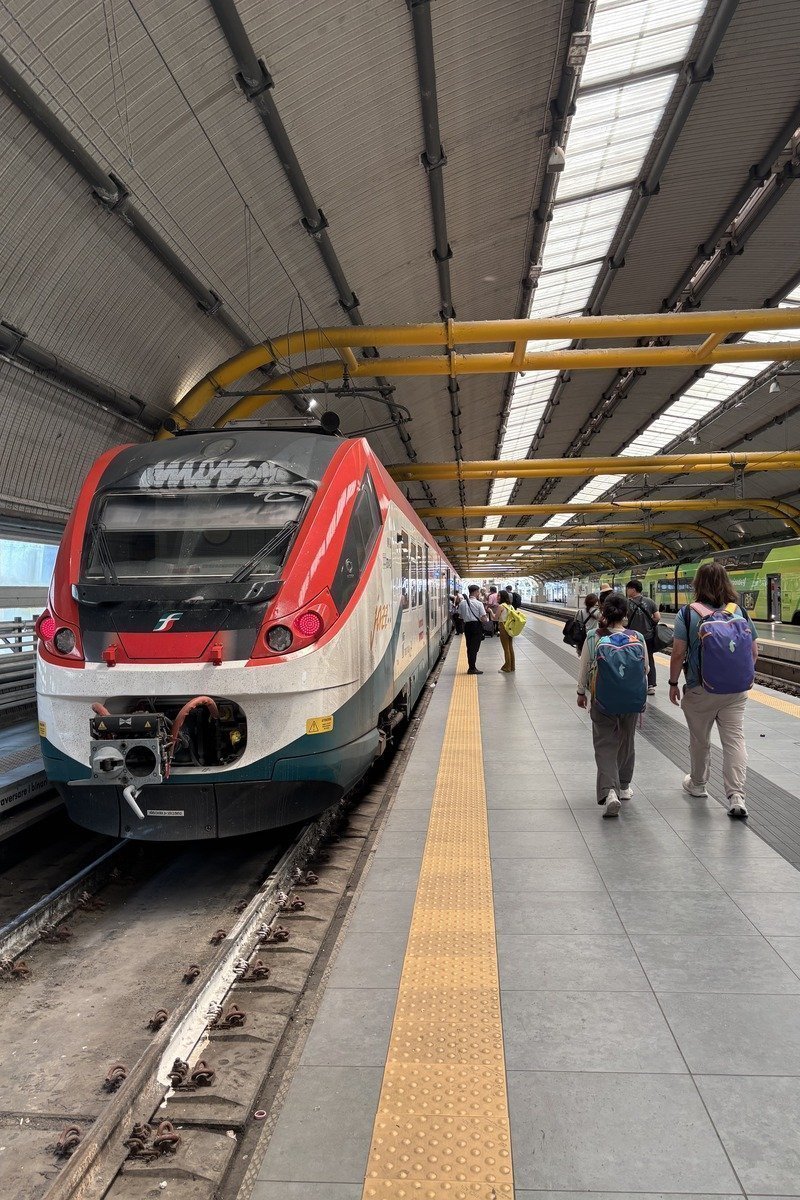Voyageurs sur un quai de gare couverte longeant un train Leonardo express