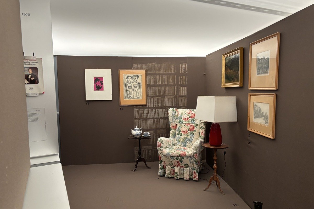 Salle d'exposition avec fauteuil fleuri, lampe rouge et tableaux encadrés