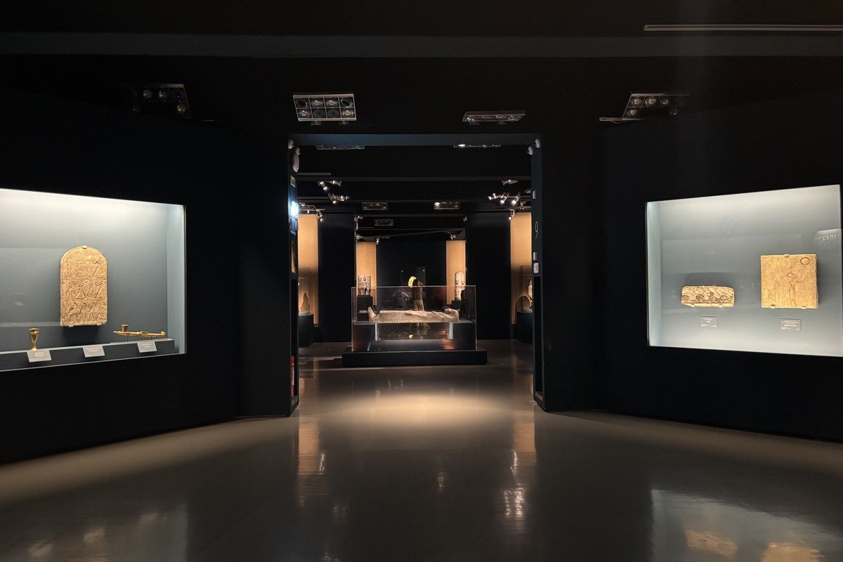 Salle de musée sombre avec vitrines illuminées présentant des artefacts anciens