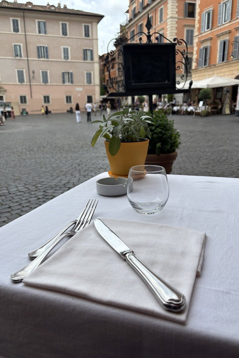 Table dressée en terrasse avec couverts, verre et plantes aromatiques