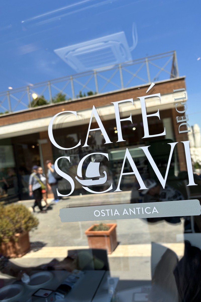 Logo blanc d'un café sur vitre, terrasse ensoleillée en arrière-plan