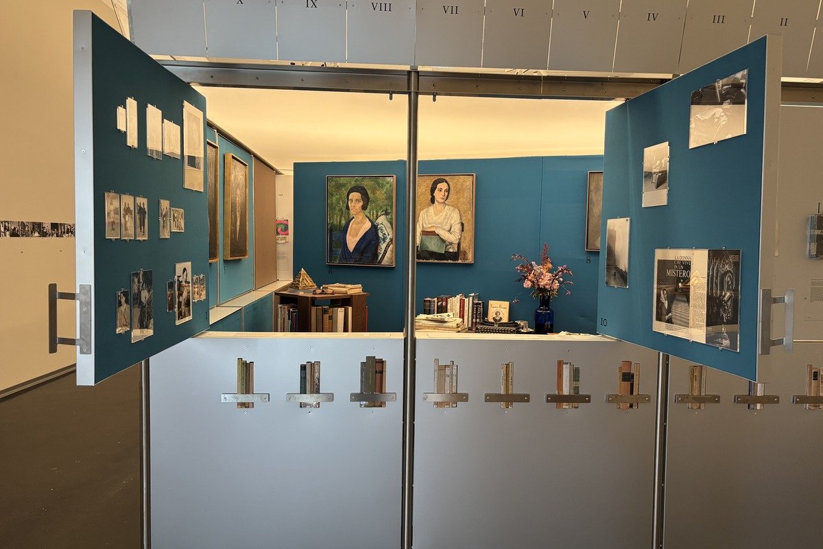 Vitrine d'exposition ouverte avec portraits peints, photos et livres
