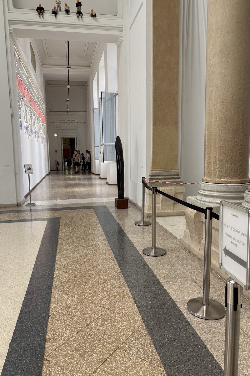 Couloir de musée avec colonnes, barrières de guidage et visiteurs au fond