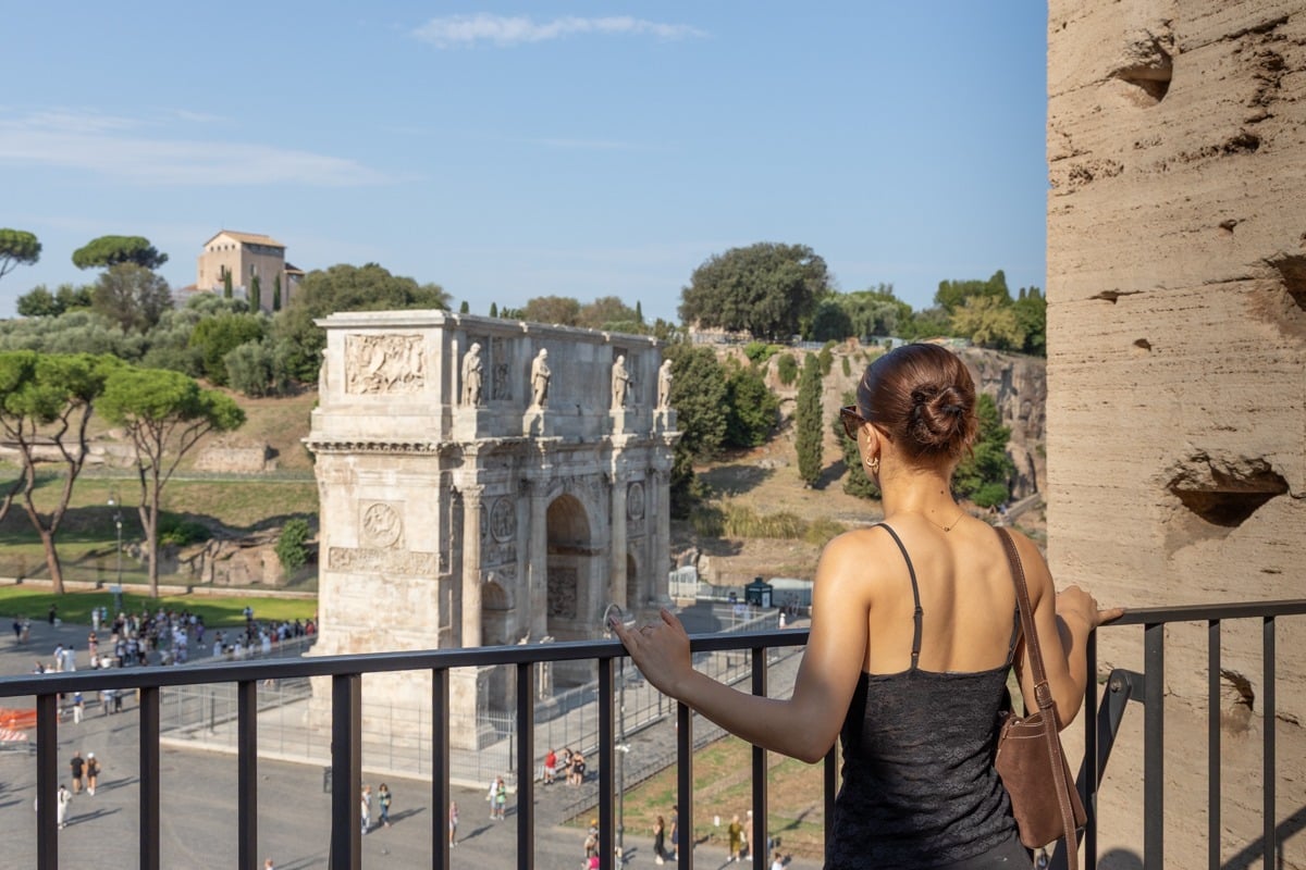 Femme de dos admirant un arc de triomphe antique depuis une terrasse