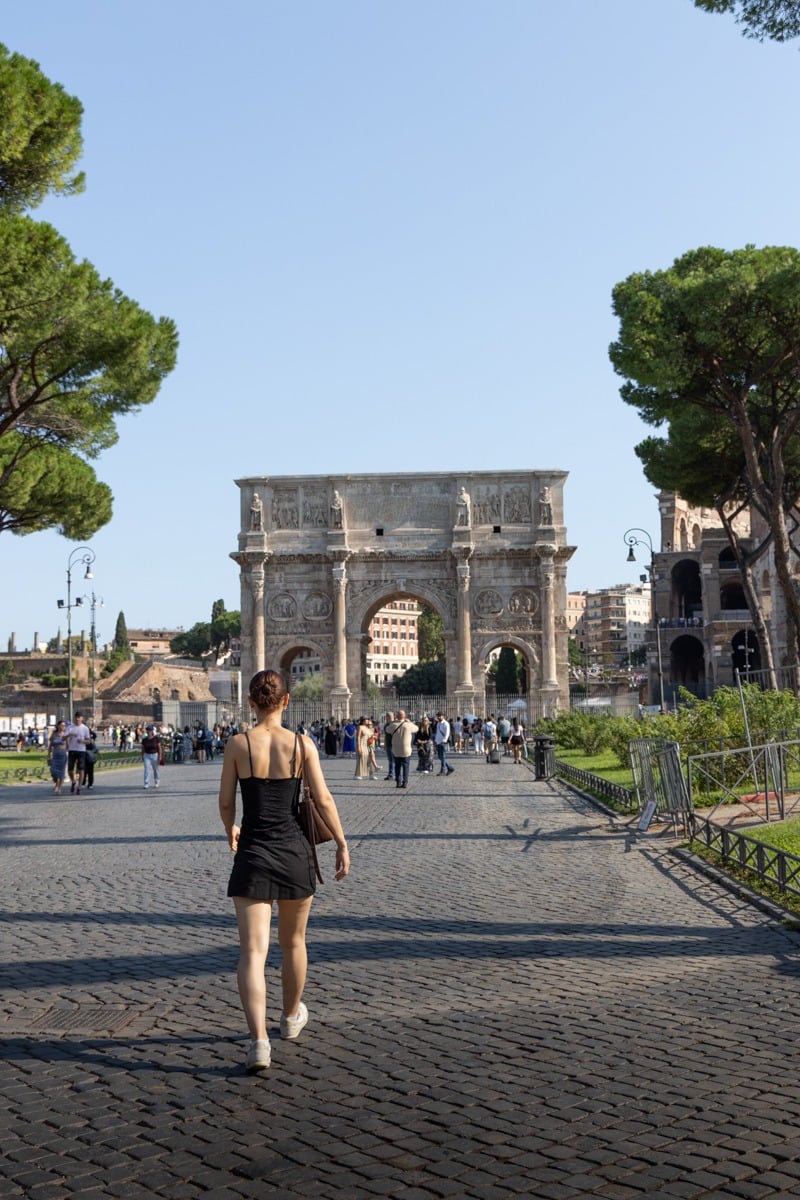 Femme de dos en robe noire marchant vers un arc de triomphe antique