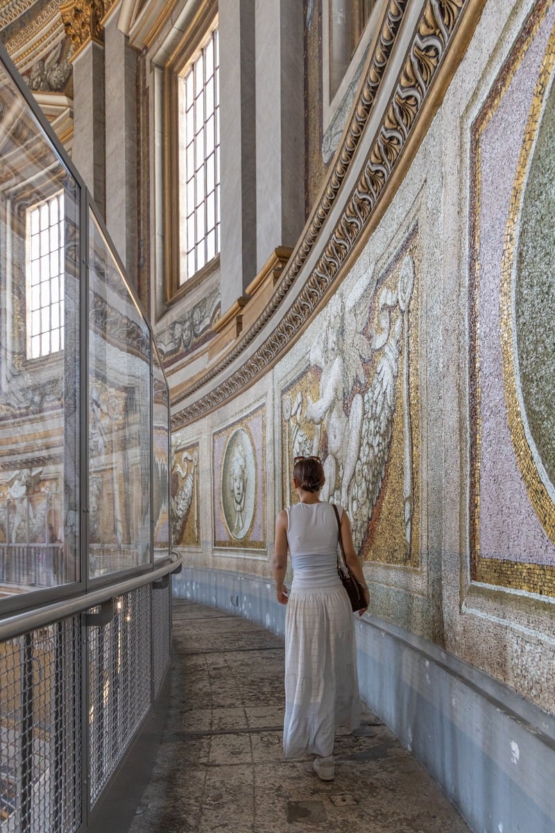 Femme en blanc admirant une mosaïque dorée dans un couloir courbe