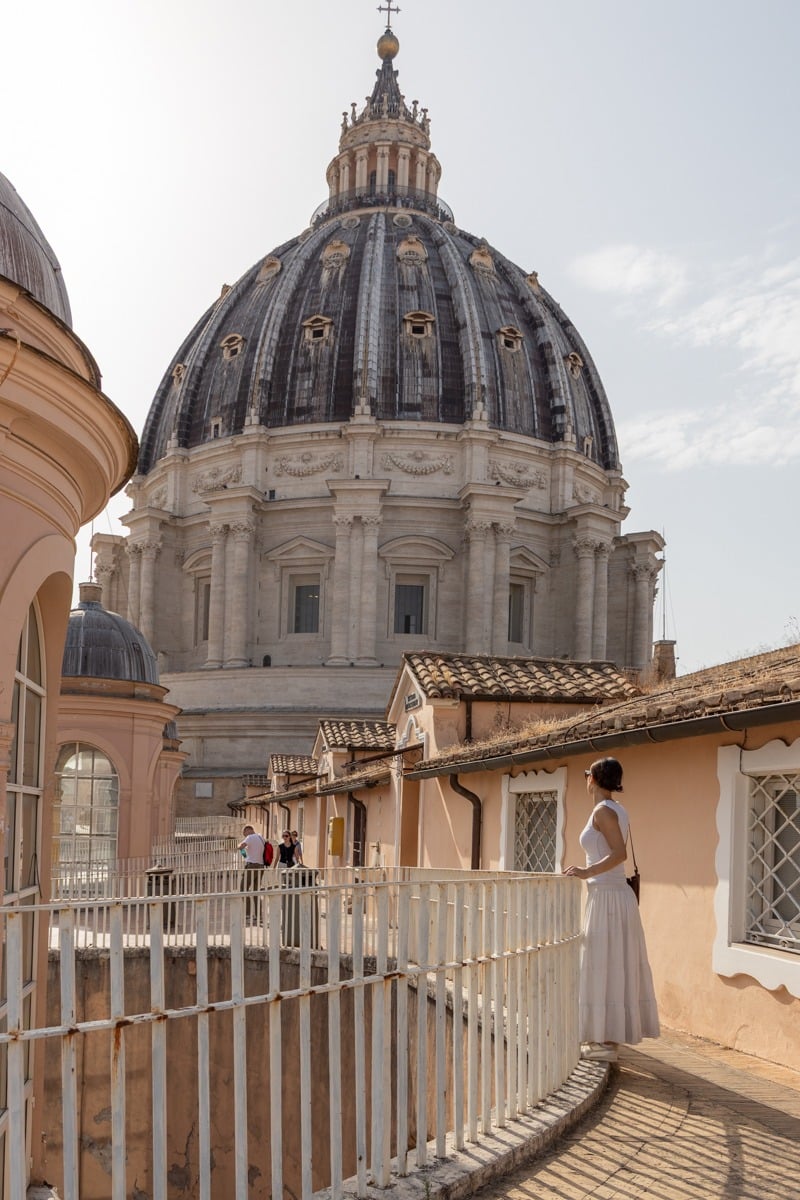 Femme en robe blanche contemplant une imposante coupole baroque depuis une terrasse