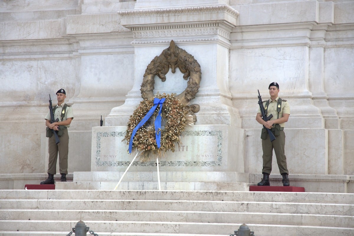 Deux soldats en uniforme encadrant une couronne dorée sur un monument