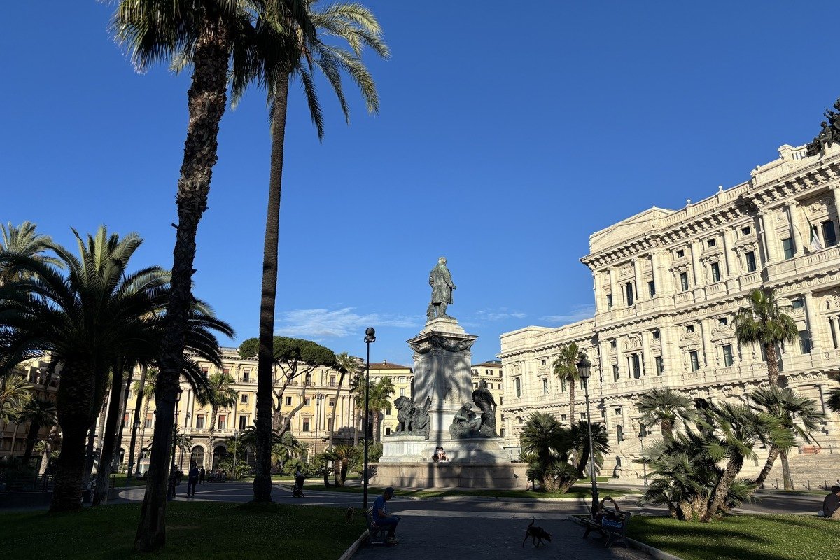 Place ensoleillée avec palmiers, statue centrale et bâtiment néoclassique