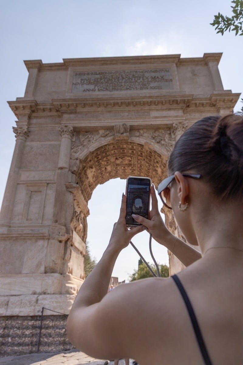 Femme de dos photographiant un arc de triomphe antique avec son smartphone