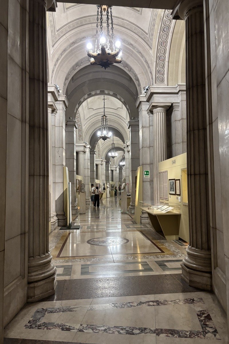 Couloir en marbre avec colonnes et voûtes, vitrines d'exposition au fond