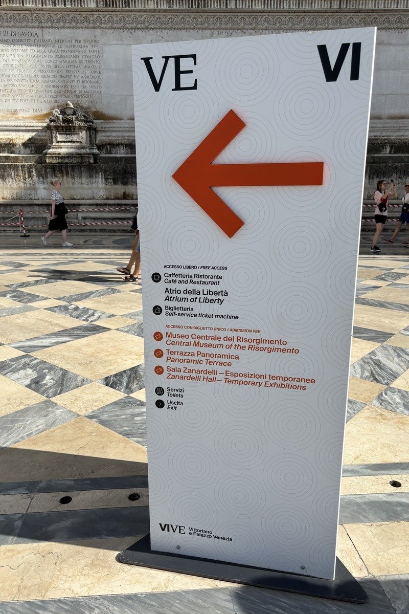 Panneau de signalétique blanc avec flèche orange indiquant les directions du musée