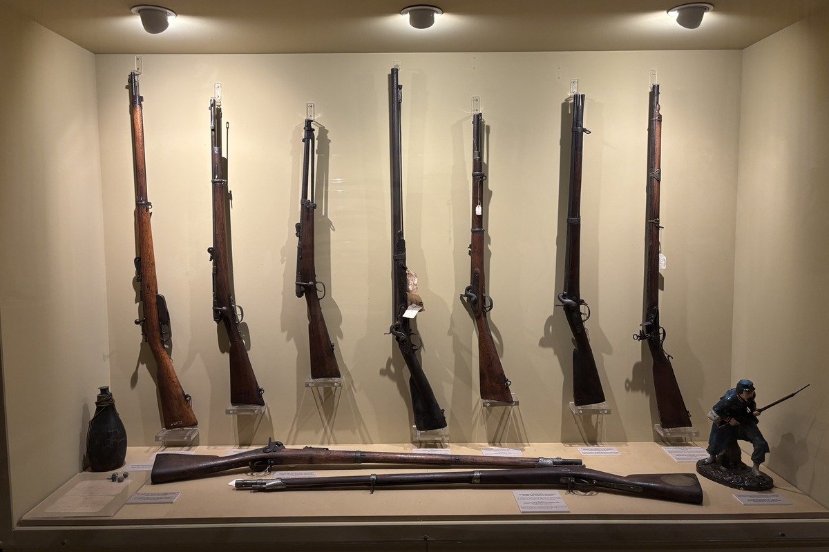Vitrine de musée présentant sept fusils anciens sur présentoirs