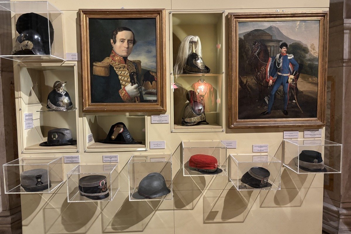 Vitrines de musée exposant casques et coiffures militaires anciens avec portraits peints